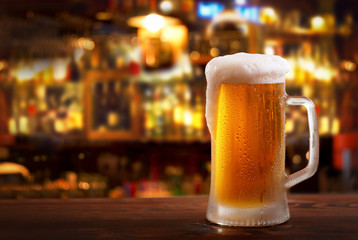 cold mug of beer in a bar on wooden table - obrazy, fototapety, plakaty