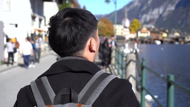Young Asian man tourist shopping and looking at souvenirs in Hallstatt Lake in Salzkammergut during trip to Austria. Traveling backpacker in Europe