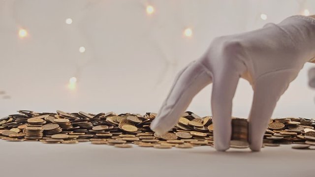White-gloved hands scooping up a pile of gold coins. They sort out and scatter money.On white background. Garland. Money glitters.