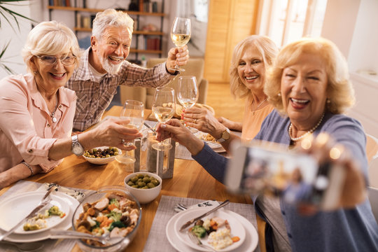 Group of cheerful seniors taking selfie at dining table.