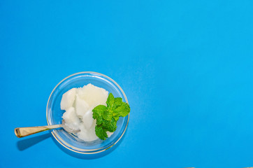 White ice cream sorbet with fresh mint leaves in glass  on blue background, refreshing summer diet dessert, top view copy space.