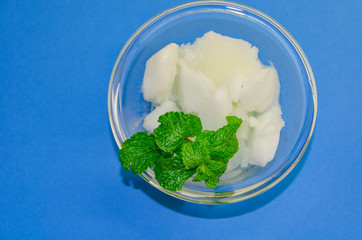 White ice cream sorbet with fresh mint leaves in glass  on blue background, refreshing summer diet dessert, top view copy space.