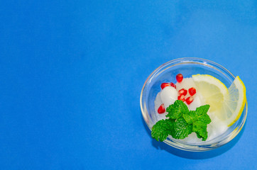 White ice cream sorbet with slice of lemon and fresh mint leaves in glass  on blue background, refreshing summer diet dessert, top view copy space.