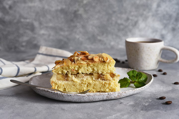 Vanilla cake with butter cream, bananas and almonds on a concrete background.
