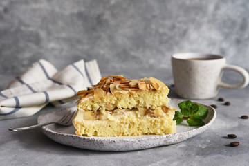 Vanilla cake with butter cream, bananas and almonds on a concrete background.