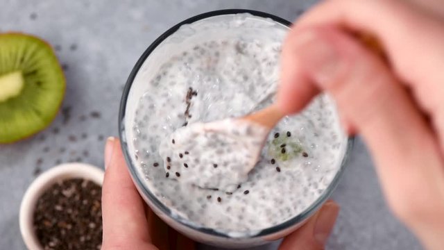 Chia seed pudding in glass jar. Female hand sprinkle black chia seeds on top of vegan chia pudding. Clean eating, healthy food