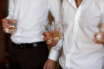 stylish friends businessmen in suits toasting with glasses of whiskey indoors, closeup. groom's morning
