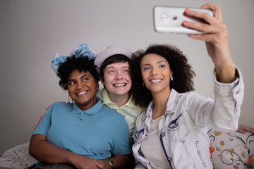 Three brazilian multiracial friends having a break for a selfie photograph all together in small apartment at living room Playful youth, enjoyment situation.