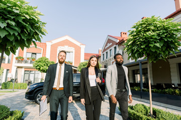 Elegant businesspeople, African and Caucasian man, Caucasian woman, walking outdoors on the yard of modern office business center.