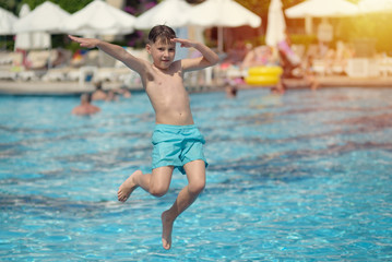 Caucasian boy having fun making high jump to plunge into swimming pool at resort.