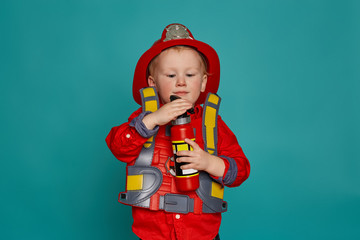 A little boy in a fireman costume plays and dreams of putting out the fire. Fireman on a blue background.