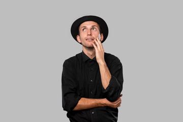 Stylish handsome man a black shirt and pork pie hat isolated over grey background.