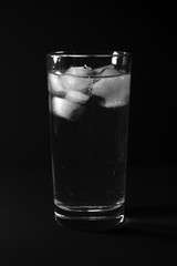 Tall flat glass with water and ice on a black background