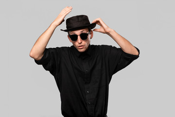 Portrait of a man in a black shirt, pork pie and sun glasses hat isolated over grey background.