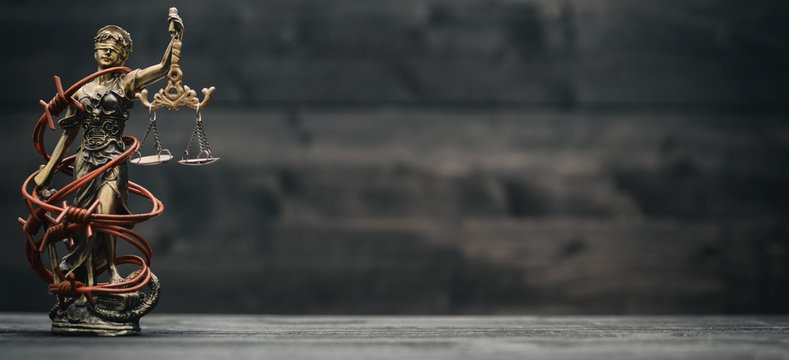 Scales of Justice, Justitia, Lady Justice and barbed wire on a black wooden background.