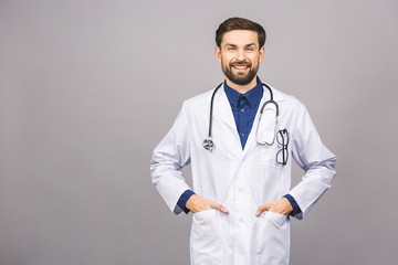 Portrait of cheerful smiling young doctor with stethoscope over neck in medical coat standing against isolated gray background.