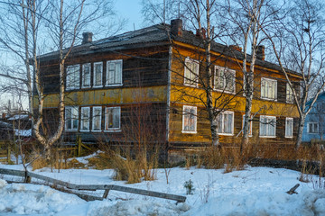 Fototapeta na wymiar Small wooden houses on a street of Rabocheostrovsky, Karelia, Russia, in winter at sunset.