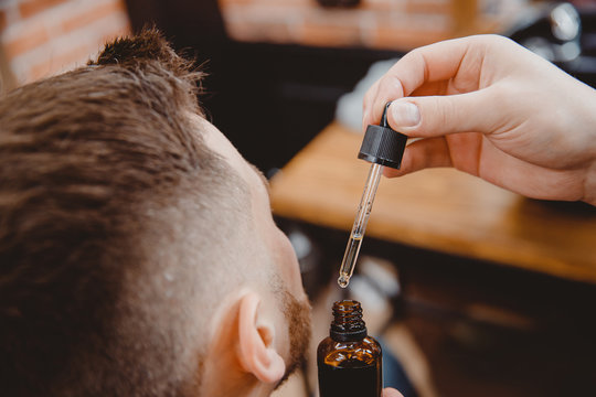 Barber Applies Beard Oil With Dropper For Man In Barbarshop