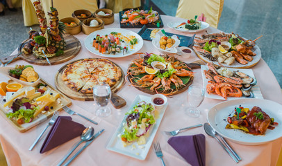dinner table with variety food, seafood, sushi, sashimi, pizza, barbeque, cheese and salad