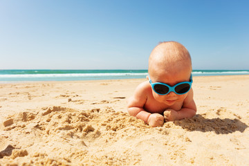 Portrait of little infant in sunglasses on a beach