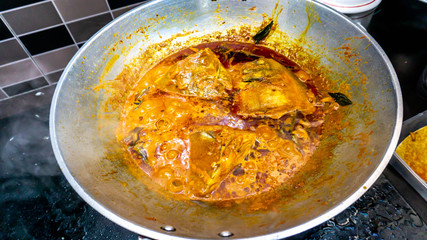 Close up view of fish head curry cooked in a metal wok on the gas stove at the house kitchen.