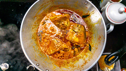 Close up view of fish head curry cooked in a metal wok on the gas stove at the house kitchen.