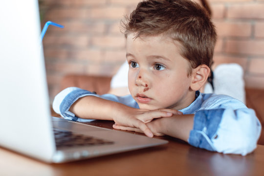 Cute blond kid attentively looking at laptop screen. Children and Technology