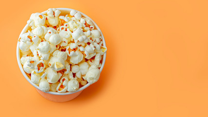 Fresh popcorn in white box on a orange background. Cinema snack concept. The food for watching a movie and entertainment. Copy space for text, top view, flat lay.