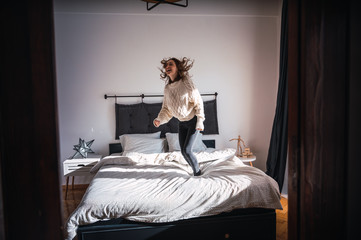 Young woman jumping in bed, happy and having fun in the morning.