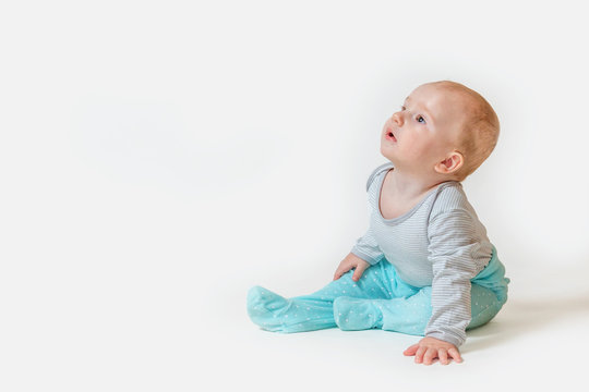 Side view of the cute baby boy sitting on white background and looking at the top left corner of the photo with a blank space for your text or product.