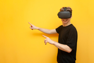guy a gamer in VR glasses on a yellow background holds a device and points his fingers to a place for text, a man with wireless gadgets for virtual reality