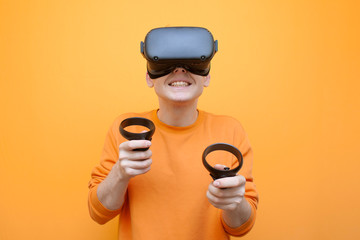 joyful guy in VR glasses on an orange background, a gamer plays a virtual game and holds modern joysticks
