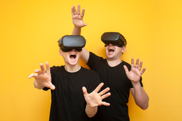 two guys in modern VR glasses play on a yellow background, a pair of friends of gamers in virtual reality glasses