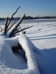 Schneebedecktes Flussufer als winterliches Idyll und Winterlandschaft l&auml;dt zum Winterspaziergang ein und zeigt Spuren im Schnee und Raureif mit Schneekristallen
