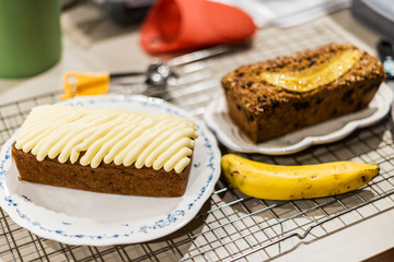 Cake decorated with cream cheese, paired with a newly baked banana cake on the table.