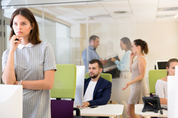 Portrait of frustrated young business woman in coworking space with working colleagues behind