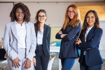 Group of confident young women looking at camera. Beautiful smiling businesswomen posing in modern office. Female confidence concept