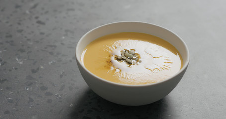 pumpkin cream soup in white bowl on terrazzo countertop