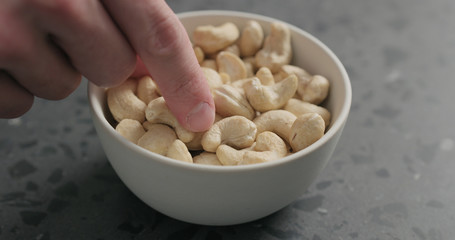 man hand takes cashew nuts from white bowl on terrazzo countertop