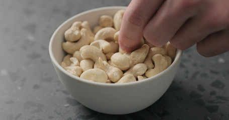 man hand takes cashew nuts from white bowl on terrazzo countertop