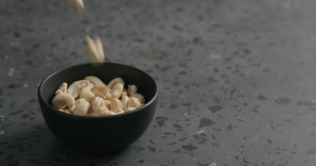 cashew nuts fall in black bowl on terrazzo countertop