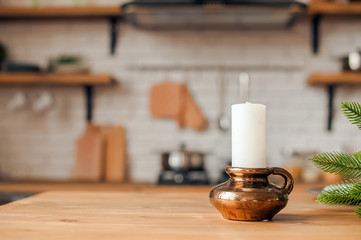 Fototapeta na wymiar Christmas kitchen decor and copy space. Rustic kitchen in defocus. Table and candle in a bronze candlestick in focus.