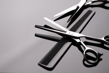Barber scissors close-up. Barber scissors and a comb lie on the mirror surface of the table. Hairdresser tool. - obrazy, fototapety, plakaty