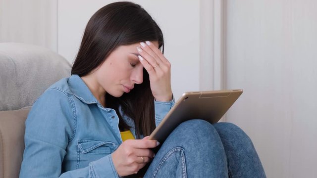 Unhappy woman sitting on floor and using tablet at home, skeptical expression, doesn't believe excuses of her unfaithful boyfriend. Lifestyle concept