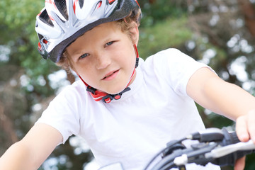 Fototapeta na wymiar Low angle view of a smiling young boy in safety helmet riding bicycle at the park in summer.