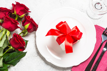 Romantic holiday table setting with plate, roses and present.