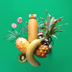 Assortment of tropical fruits around smoothie bottle on green background. Pineapple, kiwano, kiwi ,...