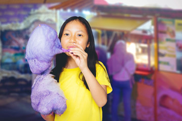 Cute girl eating a cotton candy at carnival site
