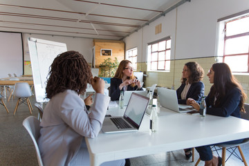 Group of professional businesswomen in meeting room. Multiethnic female colleagues sitting around...