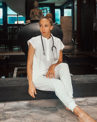 young female doctor with stethoscope on the neck on the dark background in vacation is sitting and looking away, medical travel concept, free space